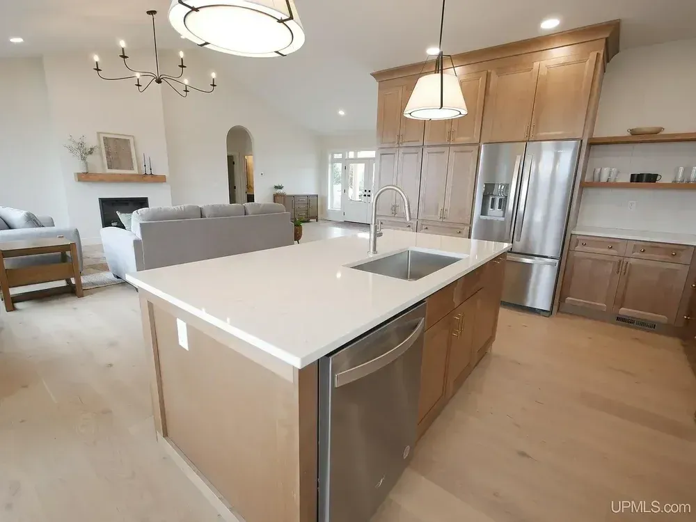 Kitchen with island, stainless steel appliances, and light wood cabinets, open to living area with fireplace.