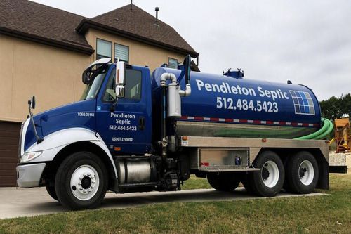 Blue Pendleton Septic tanker truck parked beside a house on grass.