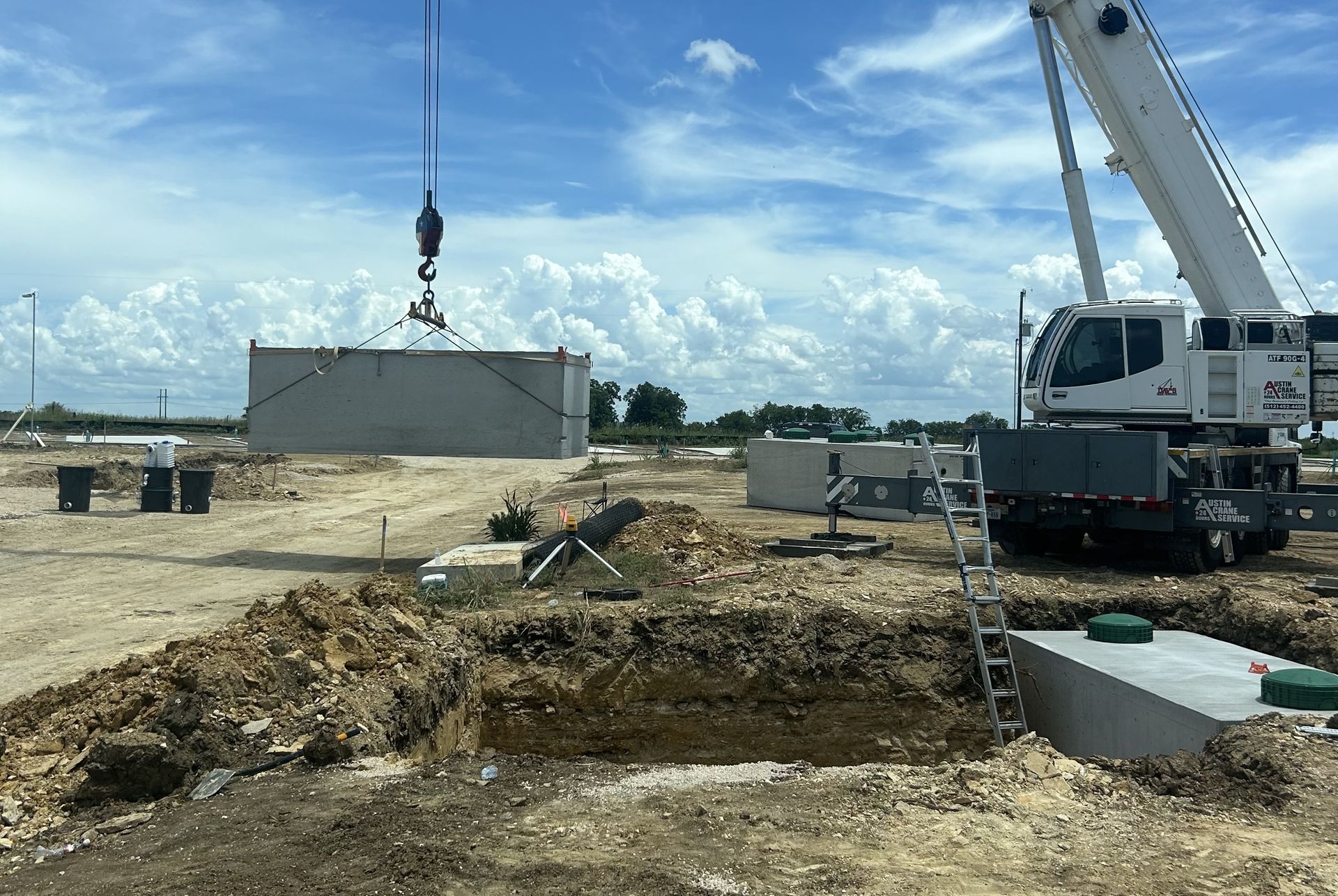 Construction site with a crane lifting a concrete panel beside a truck and piles of dirt.