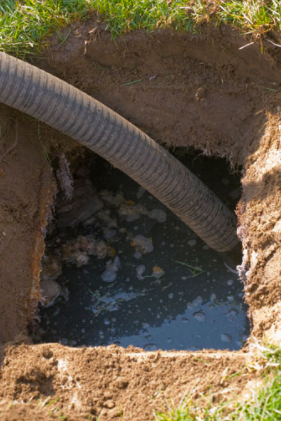 Excavation pit with muddy water and a black corrugated hose draining into it