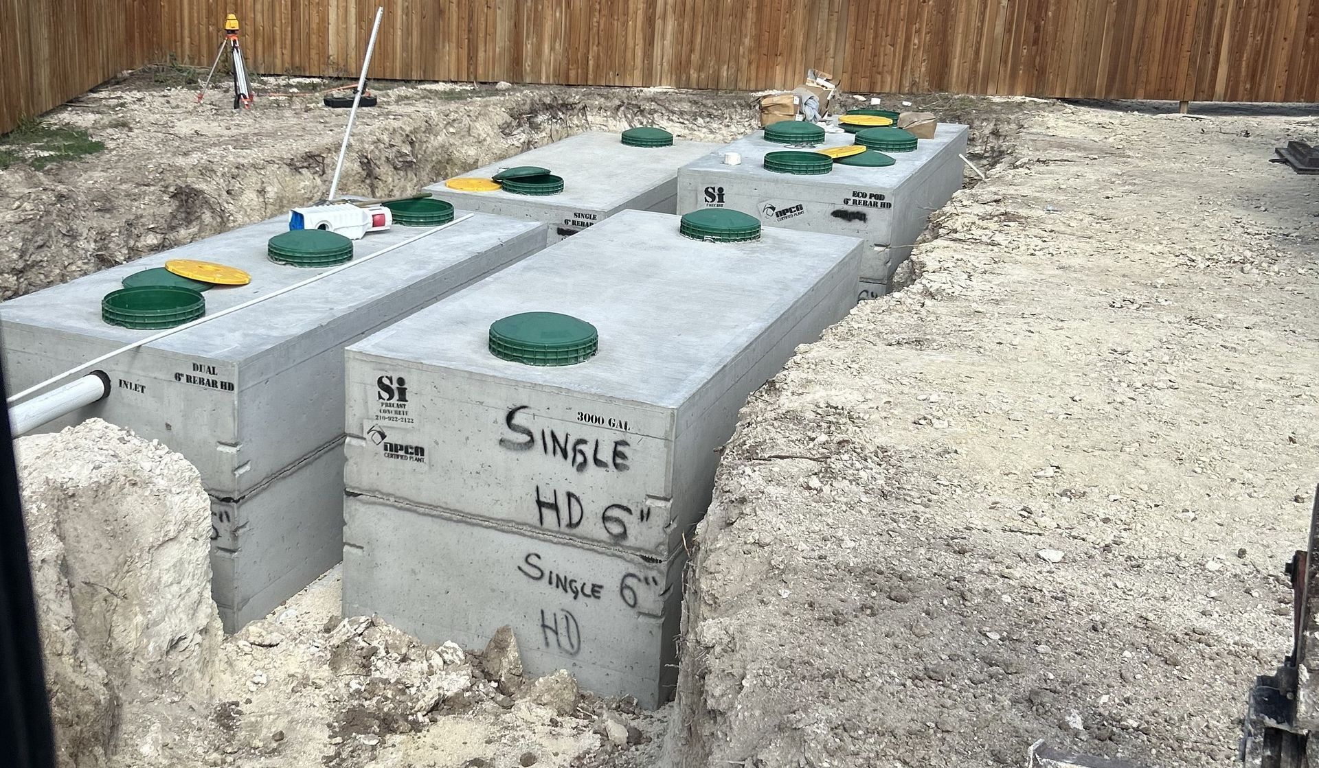 Concrete septic tank lids in a gravel yard, with one labeled “Single HD 520” and surrounded by markers.