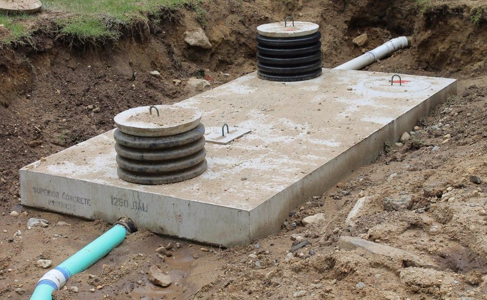 Concrete utility slab with two black vent stacks and pipes in a muddy trench