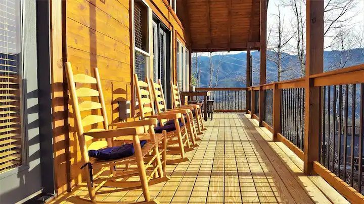 There are many rocking chairs on the porch of a cabin.