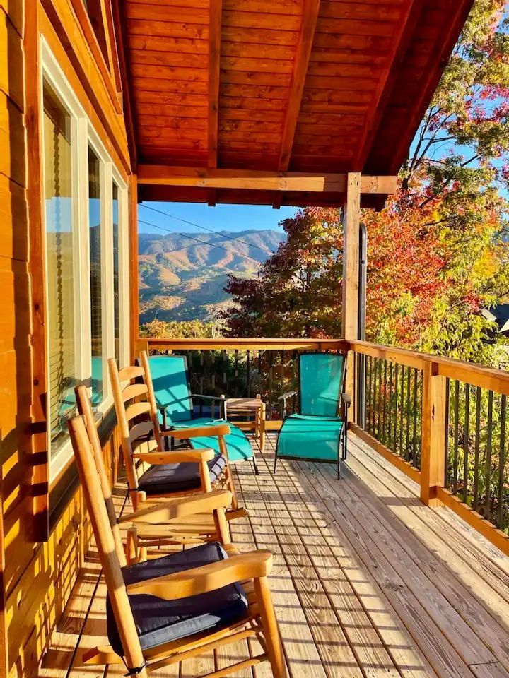 A wooden deck with rocking chairs and a view of the mountains.
