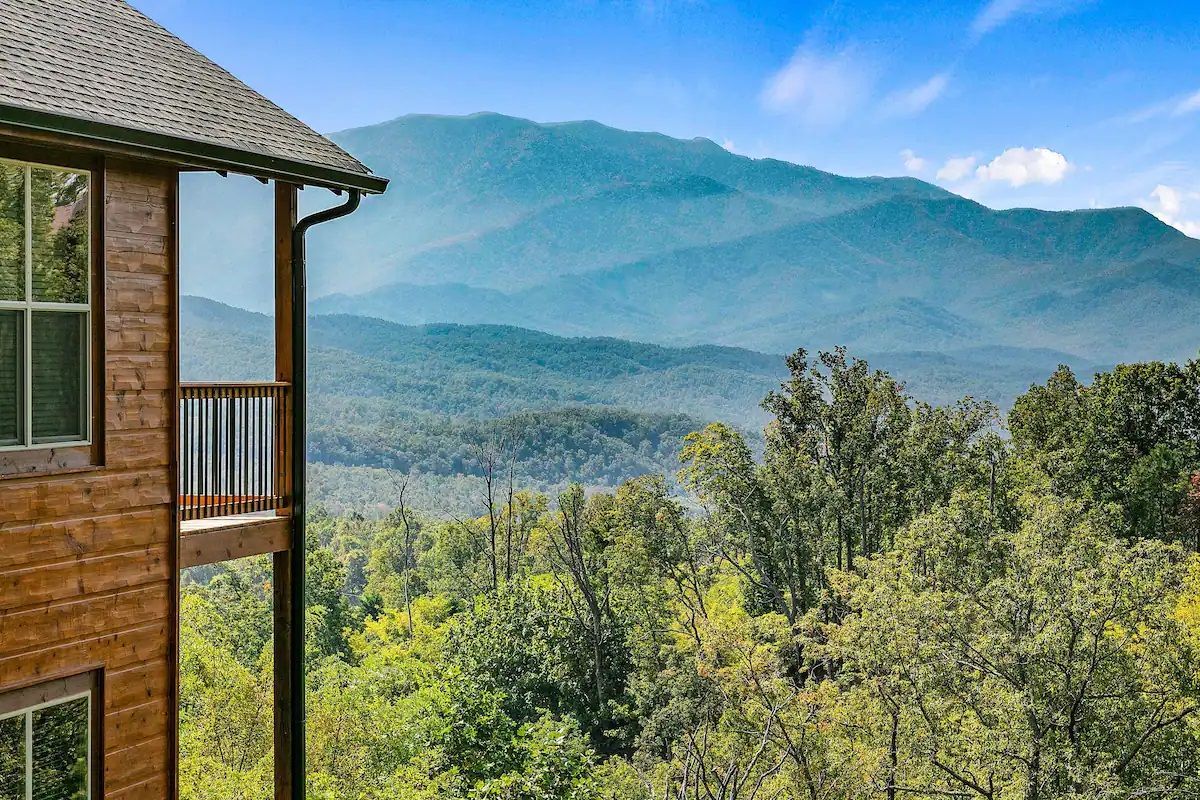 A log cabin with a view of mountains and trees.