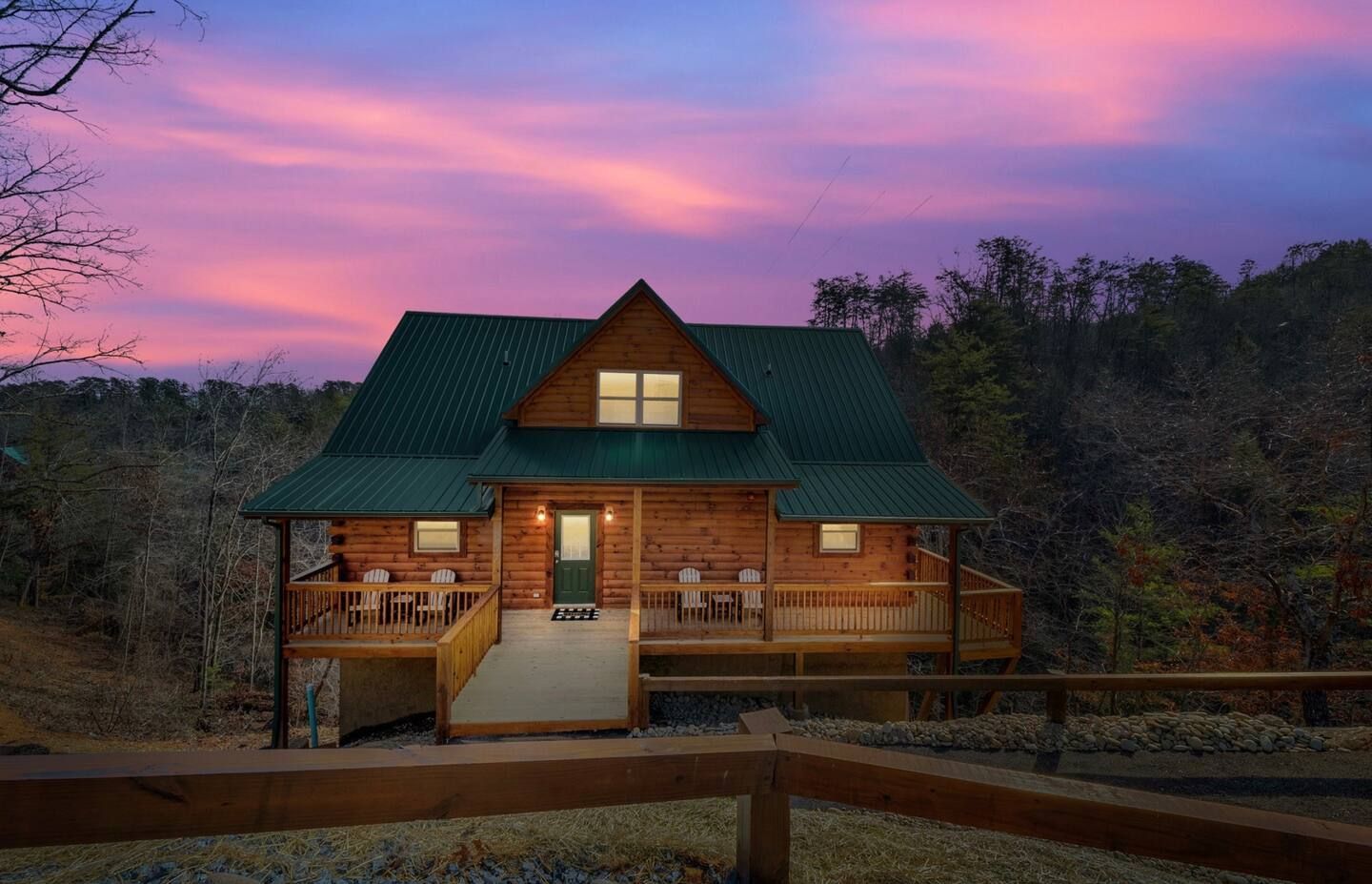 A log cabin in the middle of a forest with a sunset in the background.