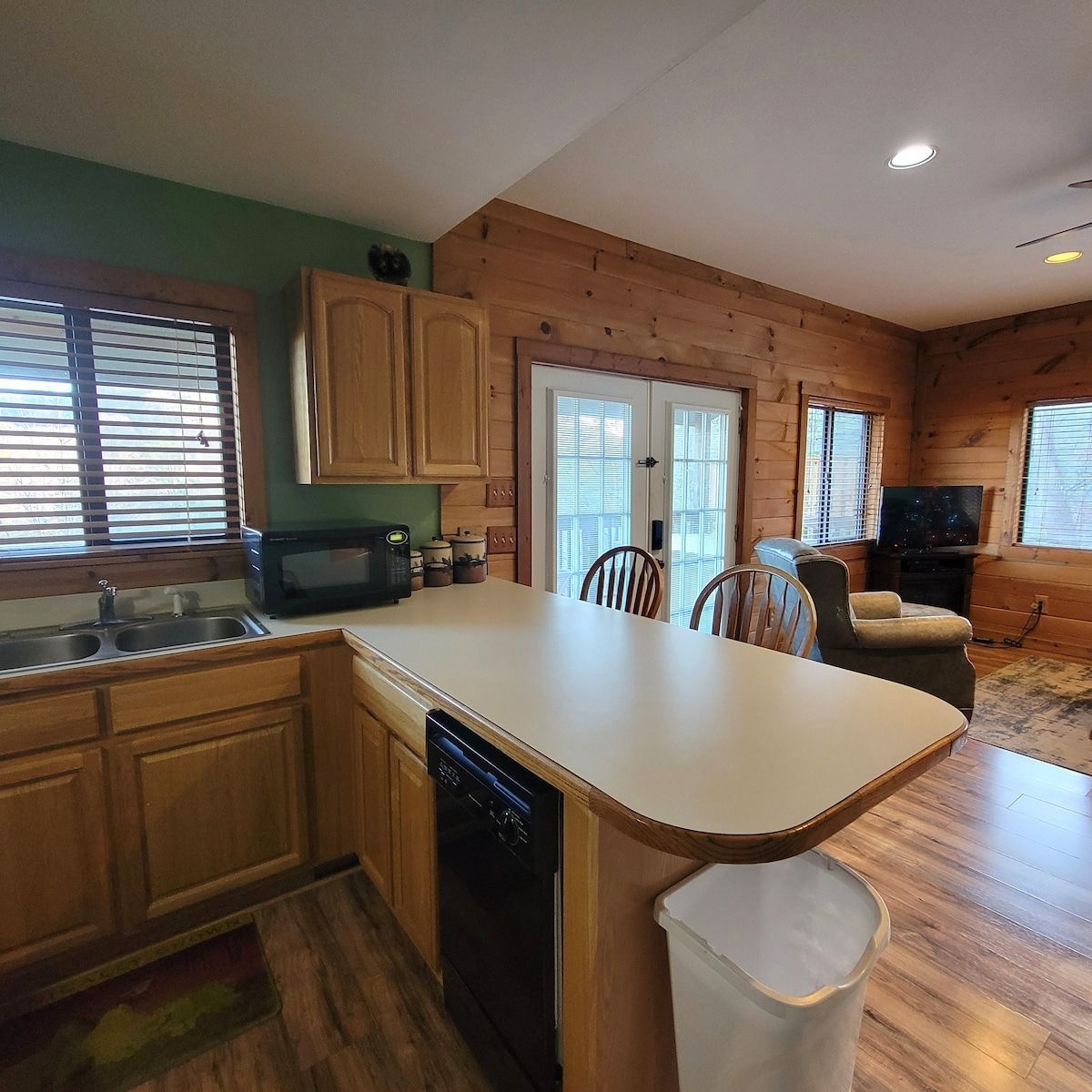 A kitchen with wooden cabinets , a sink , a microwave and a trash can.