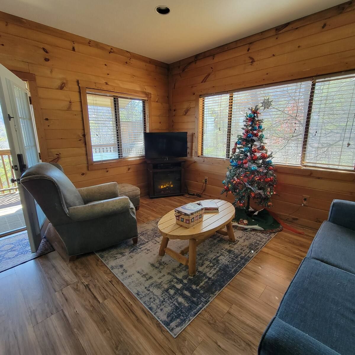 A living room with a couch , chair , coffee table and a christmas tree.