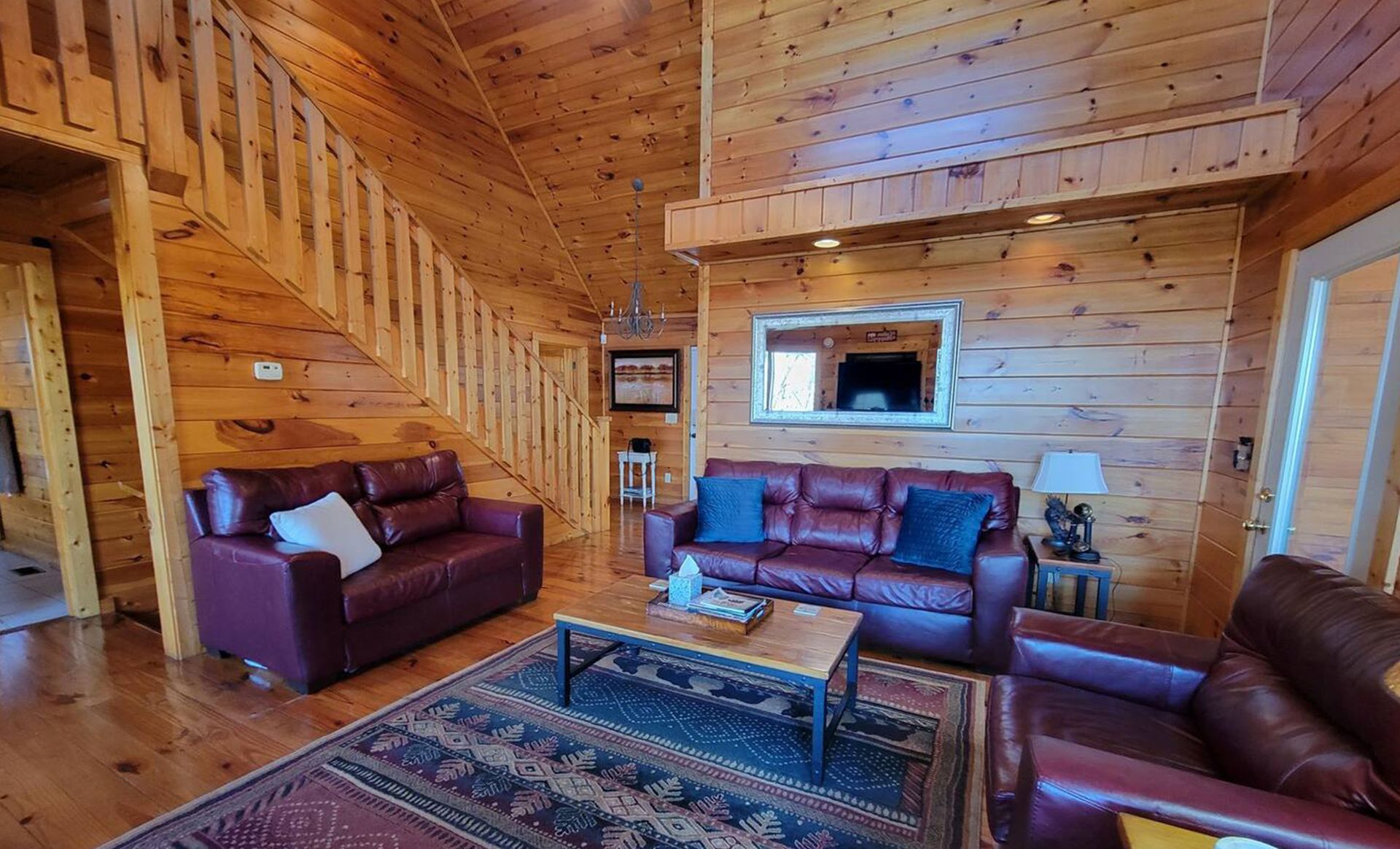 A living room in a log cabin with a couch , chair , coffee table and stairs.