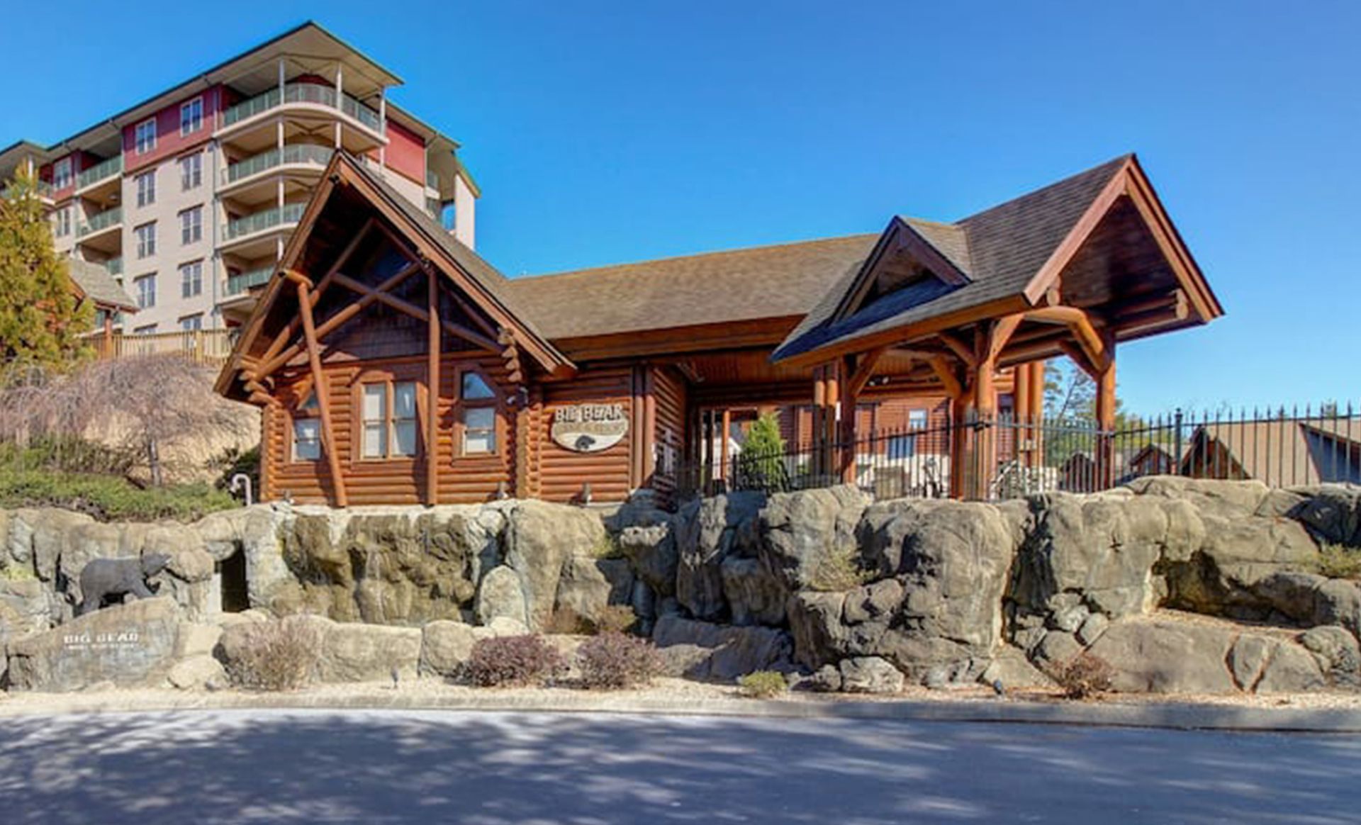 A large log cabin is sitting on top of a rocky hill next to a building.