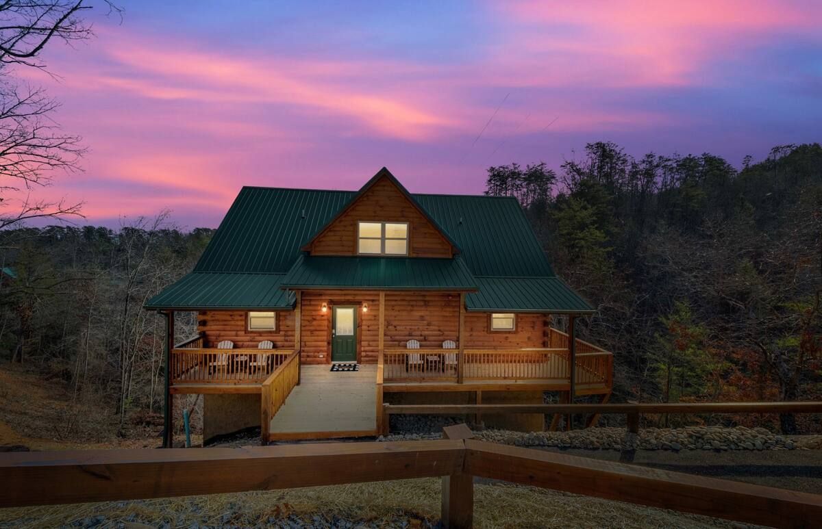 A log cabin is surrounded by trees and a fence at sunset.