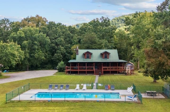 Cabin with covered porch and fenced outdoor pool surrounded by trees and lawn