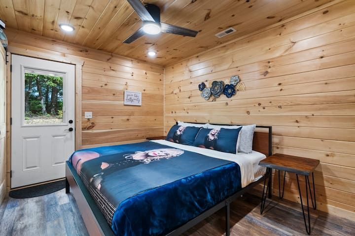 Cozy wood-paneled bedroom with a blue bedspread, ceiling fan, and windowed door to the outside