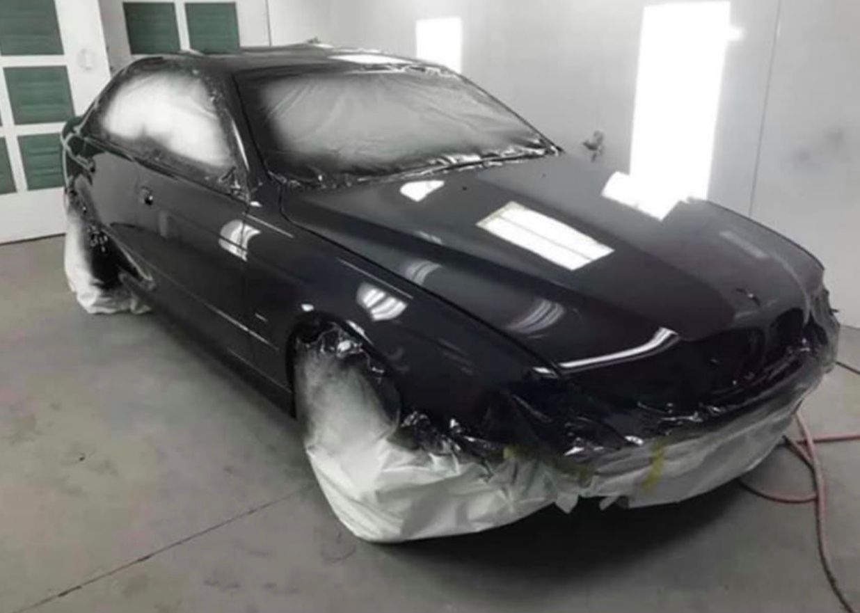 A black car is being painted in a paint booth