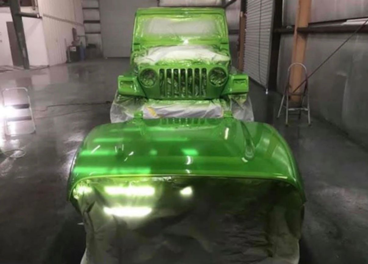 A green jeep is being painted in a garage.