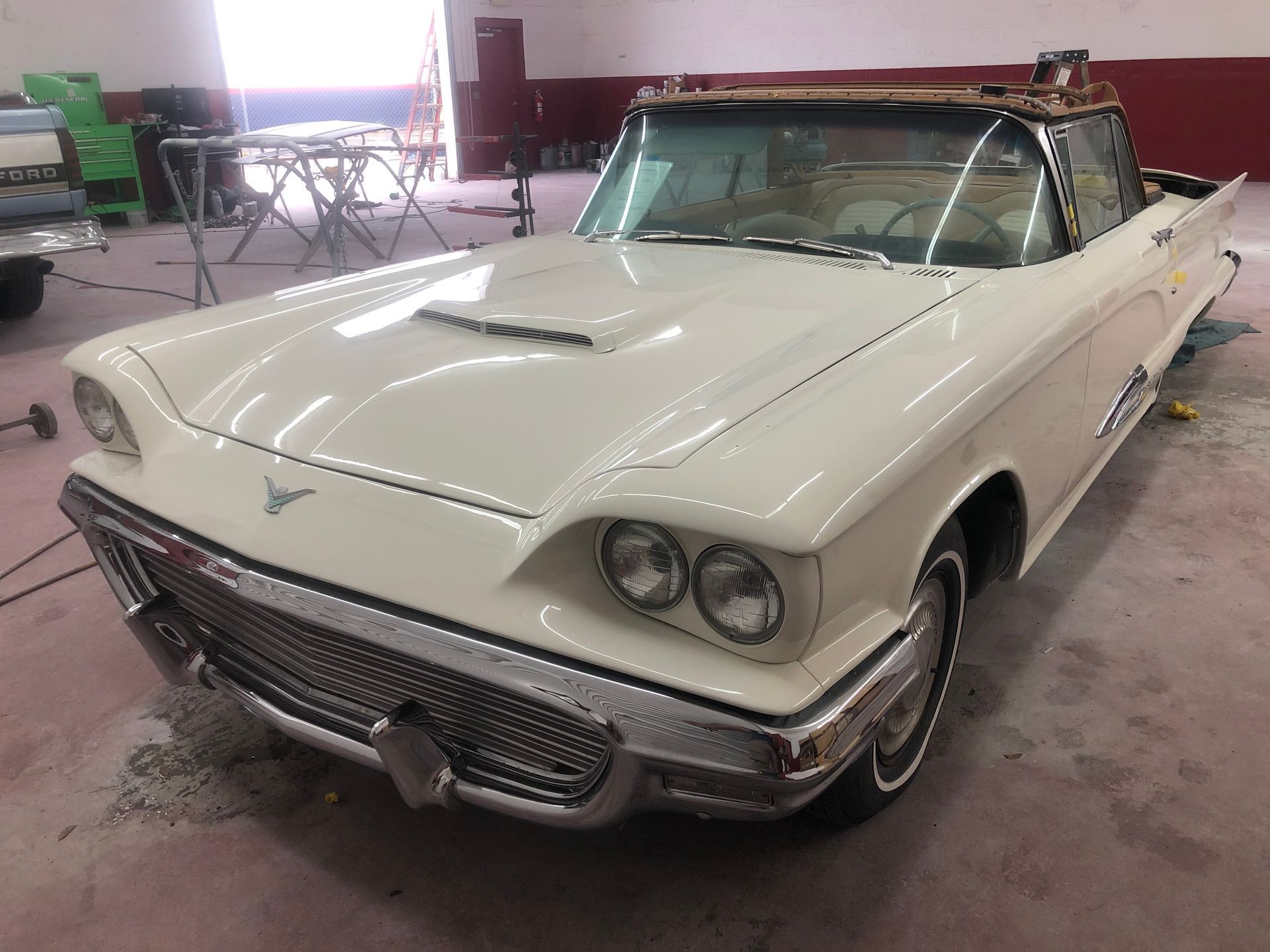 A white ford thunderbird convertible is parked in a garage.
