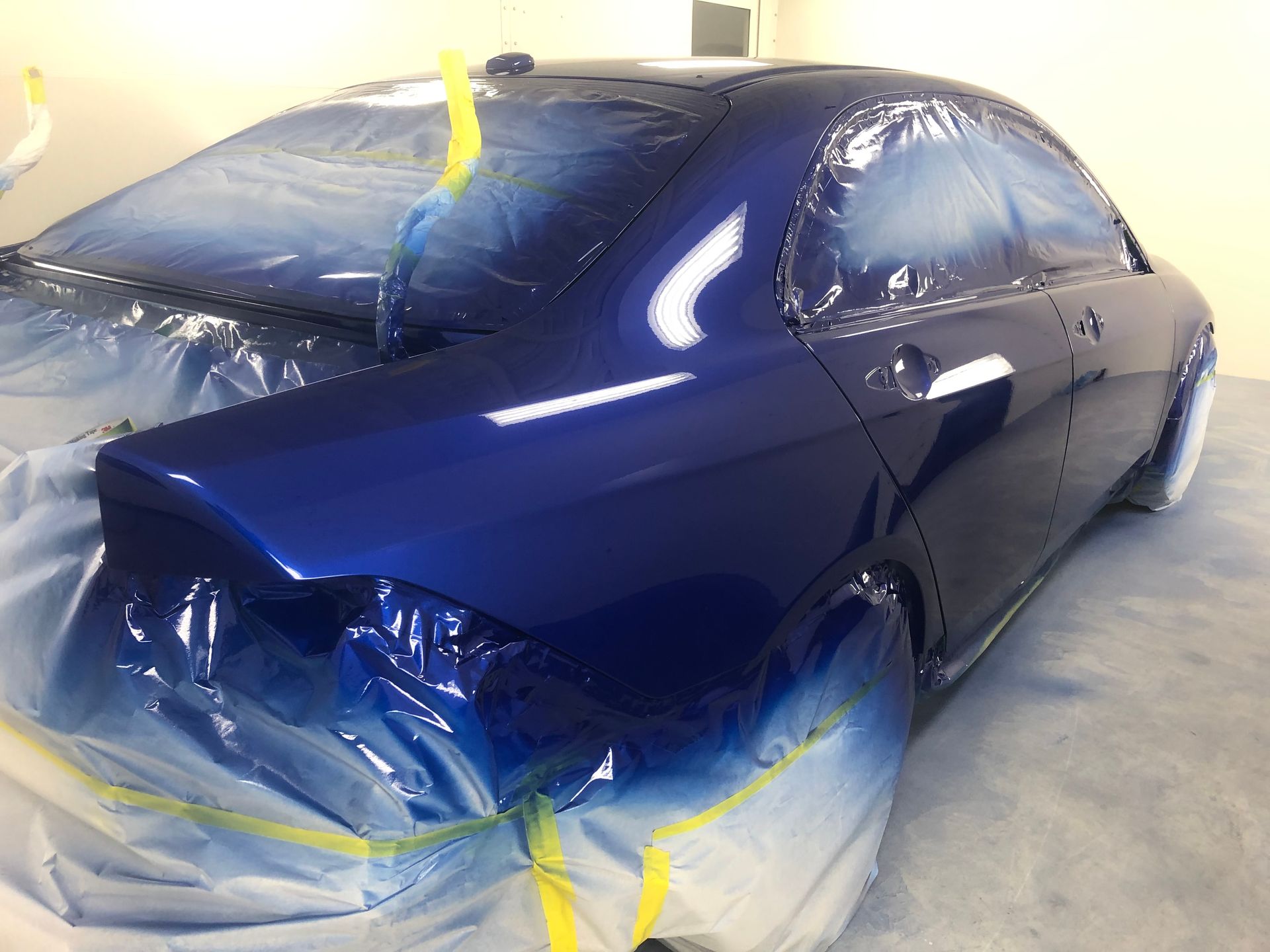 A blue car is being painted in a garage