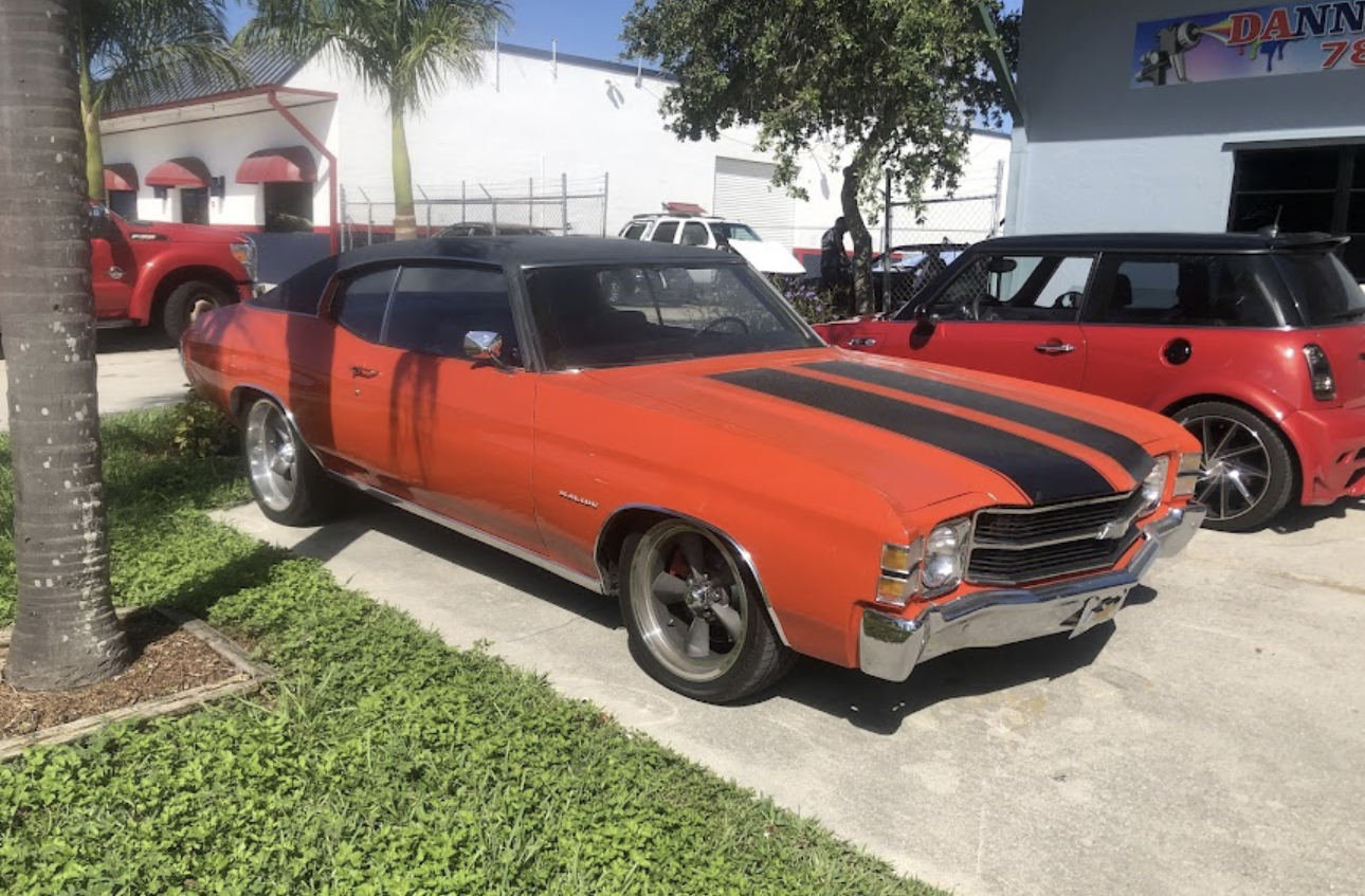 A red car with black stripes is parked in front of a building.