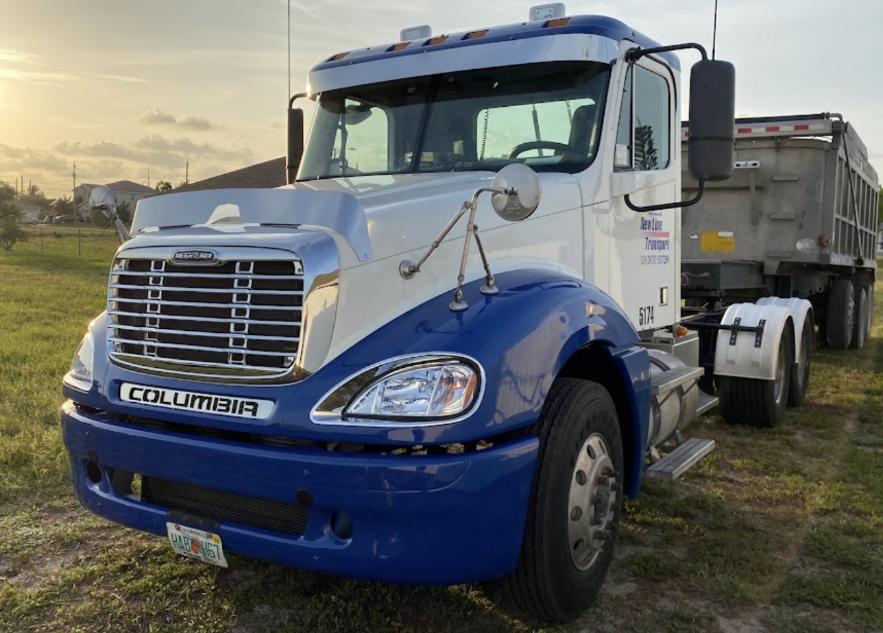 A blue and white semi truck is parked in a grassy field.