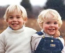 Two young children with blonde hair smiling; one in a white sweater, the other in denim overalls.