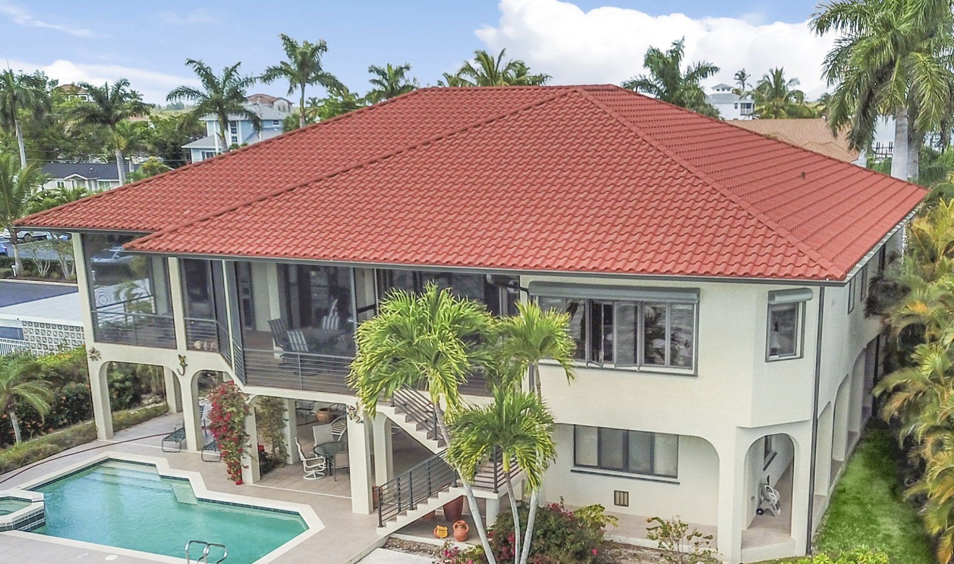 A two-story light-colored house with a red tile roof, featuring a screened-in porch and an adjacent swimming pool.