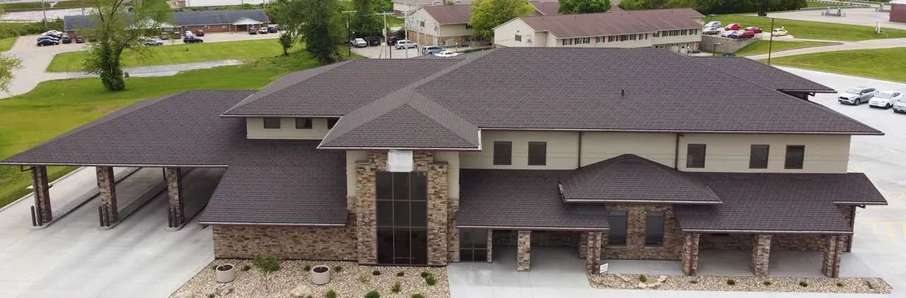 Aerial view of a single-story commercial building with a stone facade, beige walls, and dark brown shingled roofs.
