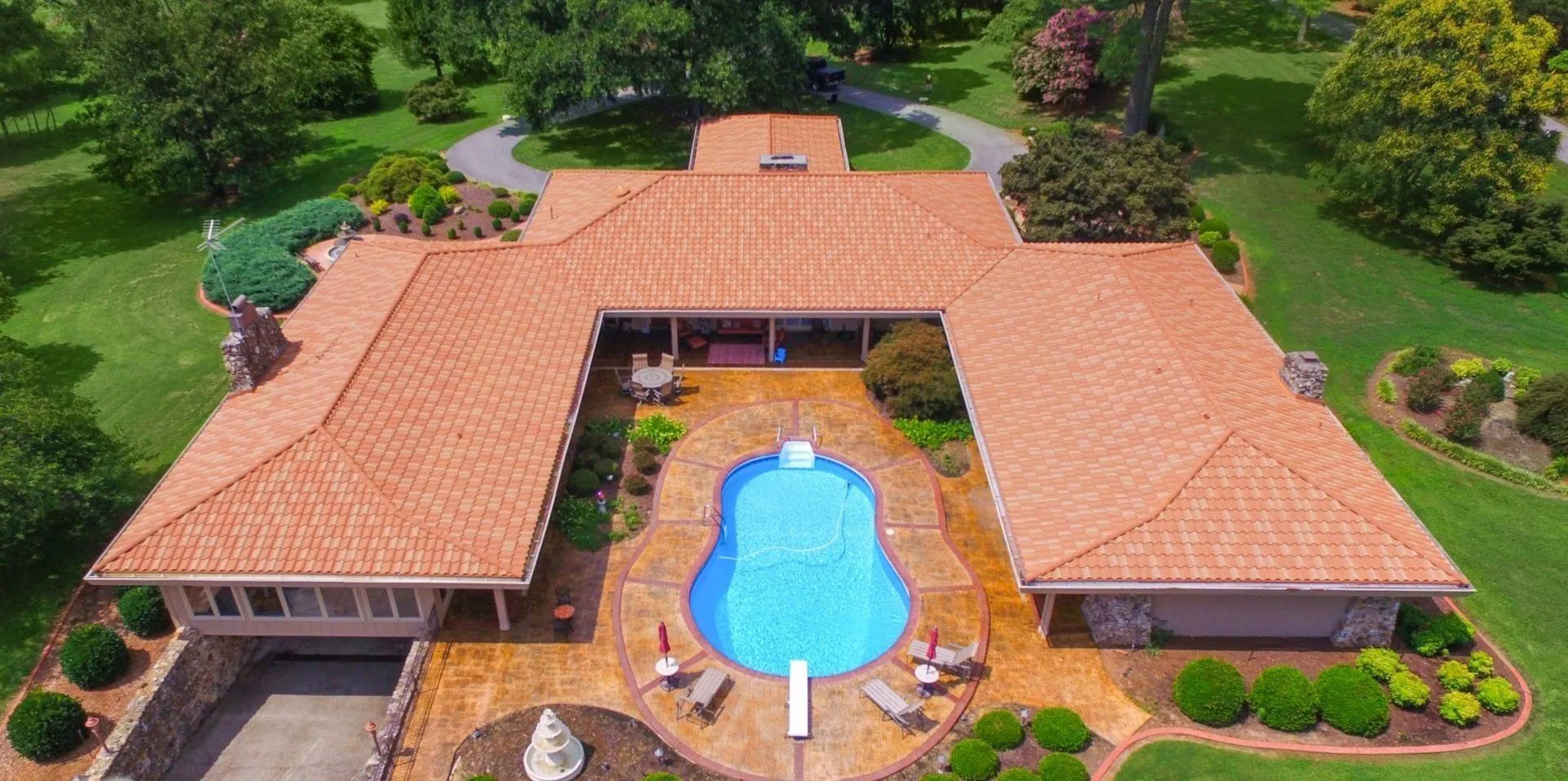 Aerial view of a U-shaped home with a terracotta roof, a central swimming pool with a diving board, and grassy grounds.