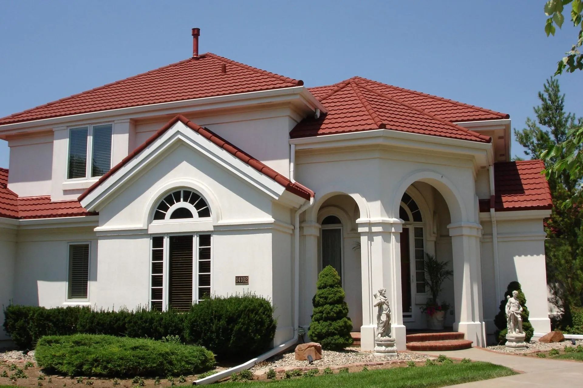A white house with a red tile roof and a covered front entryway featuring arched stone columns.