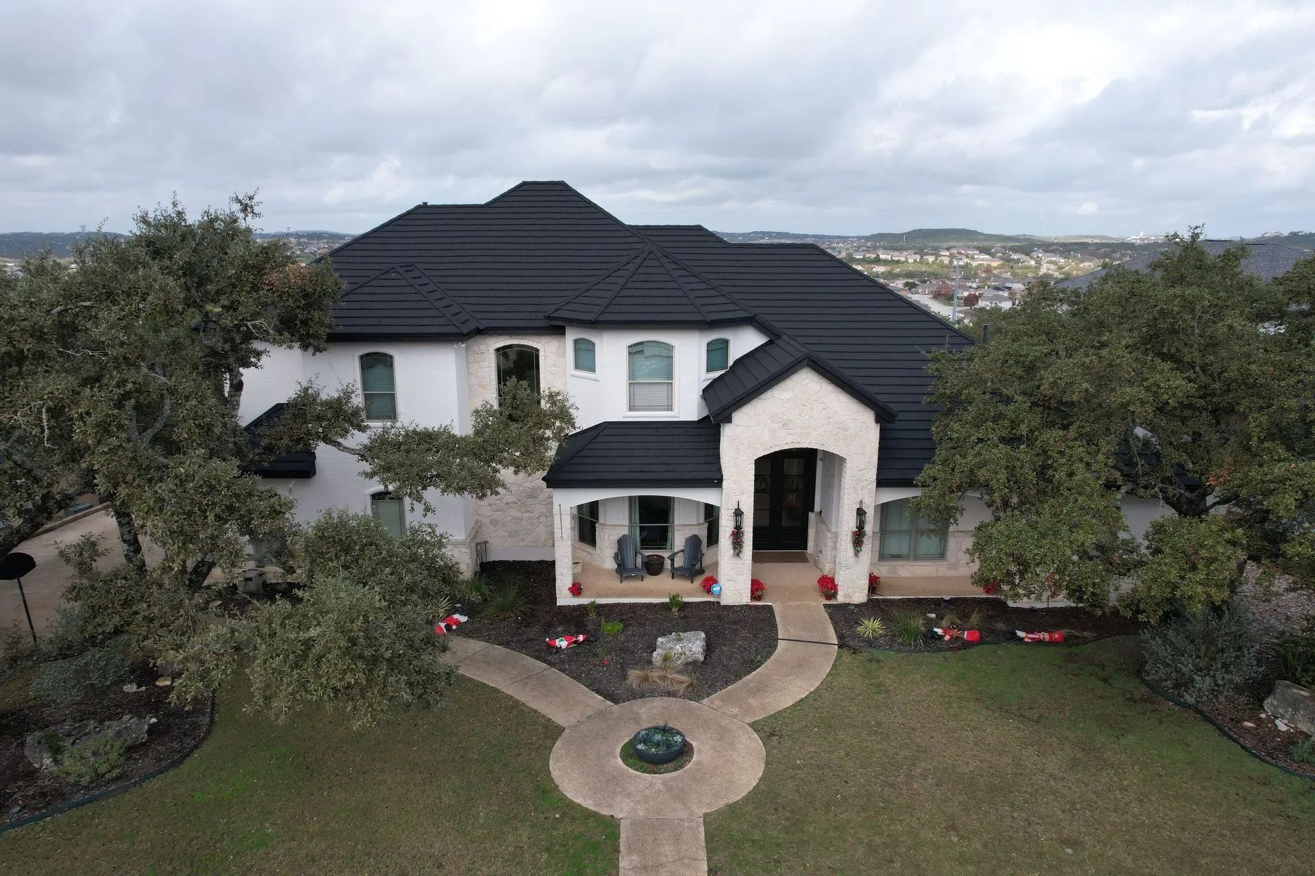 An aerial view of a two-story white house with a dark roof, surrounded by mature trees and a paved front walkway.
