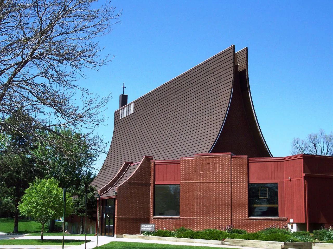 A red brick building with a tall, distinctive curved shingled roof under a clear blue sky.