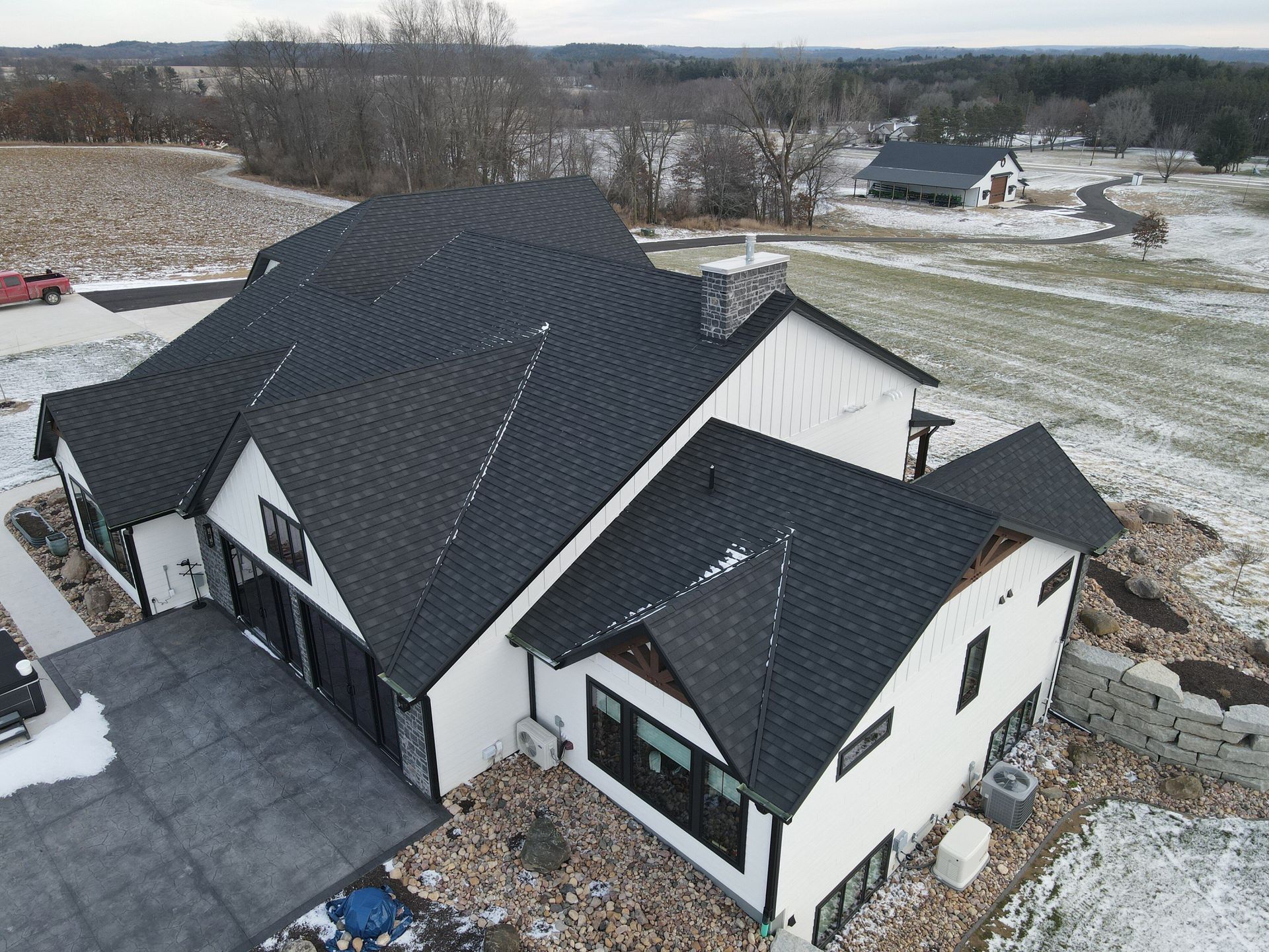 A high-angle view of a modern white house with a dark roof and black trim, surrounded by a light dusting of snow.