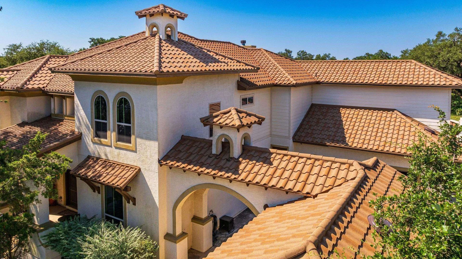 A Mediterranean-style house with off-white stucco walls and a terracotta tile roof under a clear blue sky.