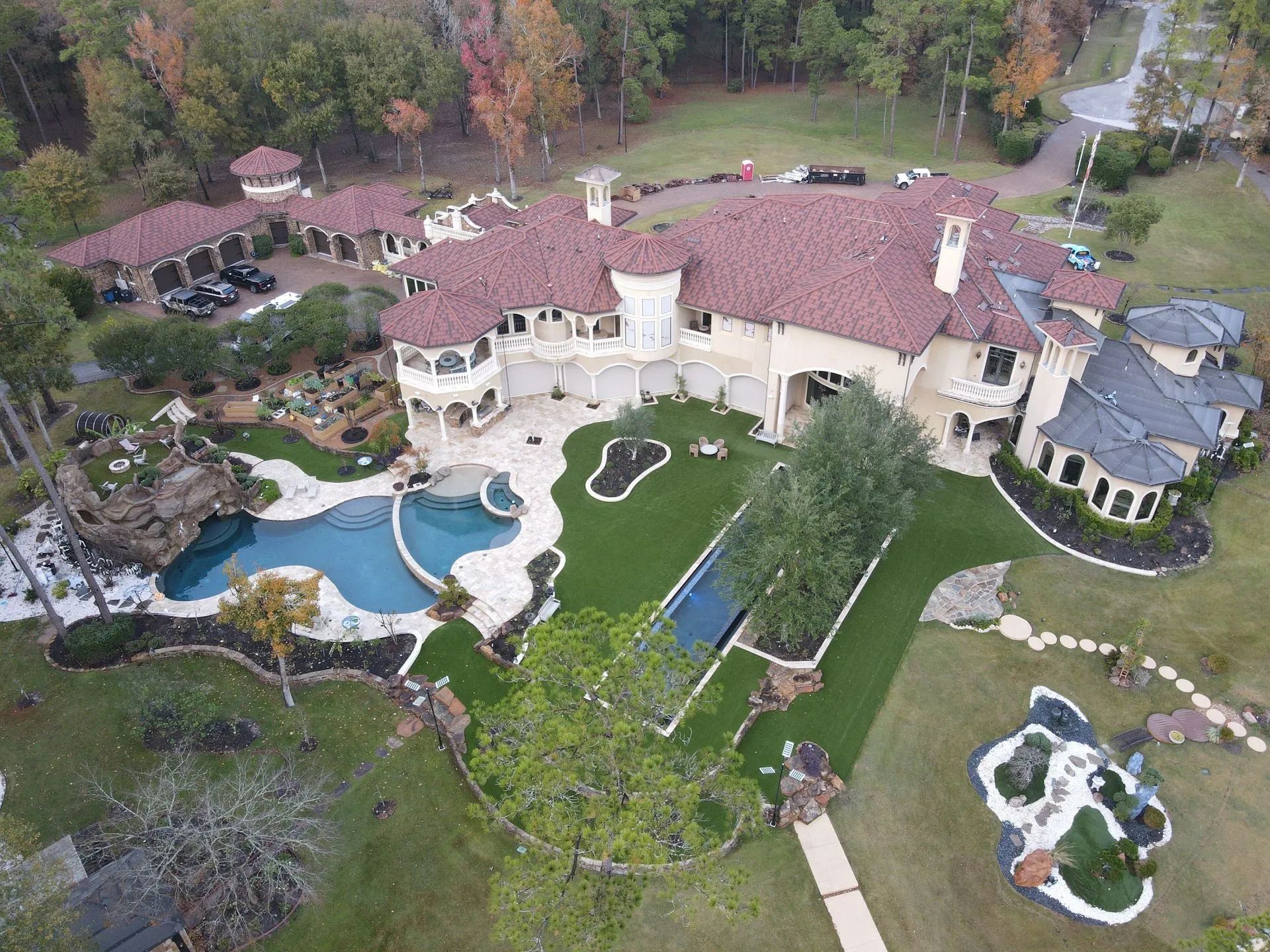 Aerial view of a sprawling luxury mansion with a red-tiled roof, multiple pools, and landscaped grounds.