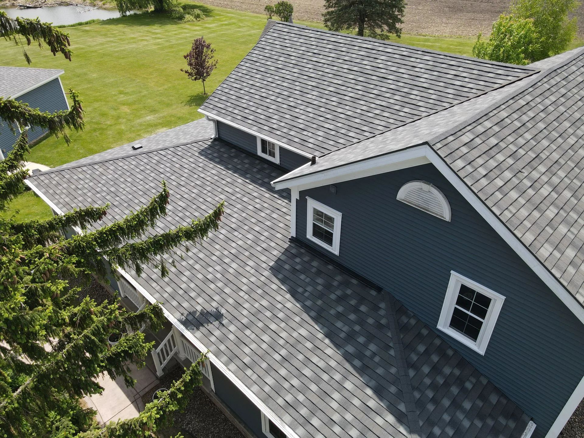 An aerial view of a dark gray shingled roof on a house with navy blue siding and white window trim.