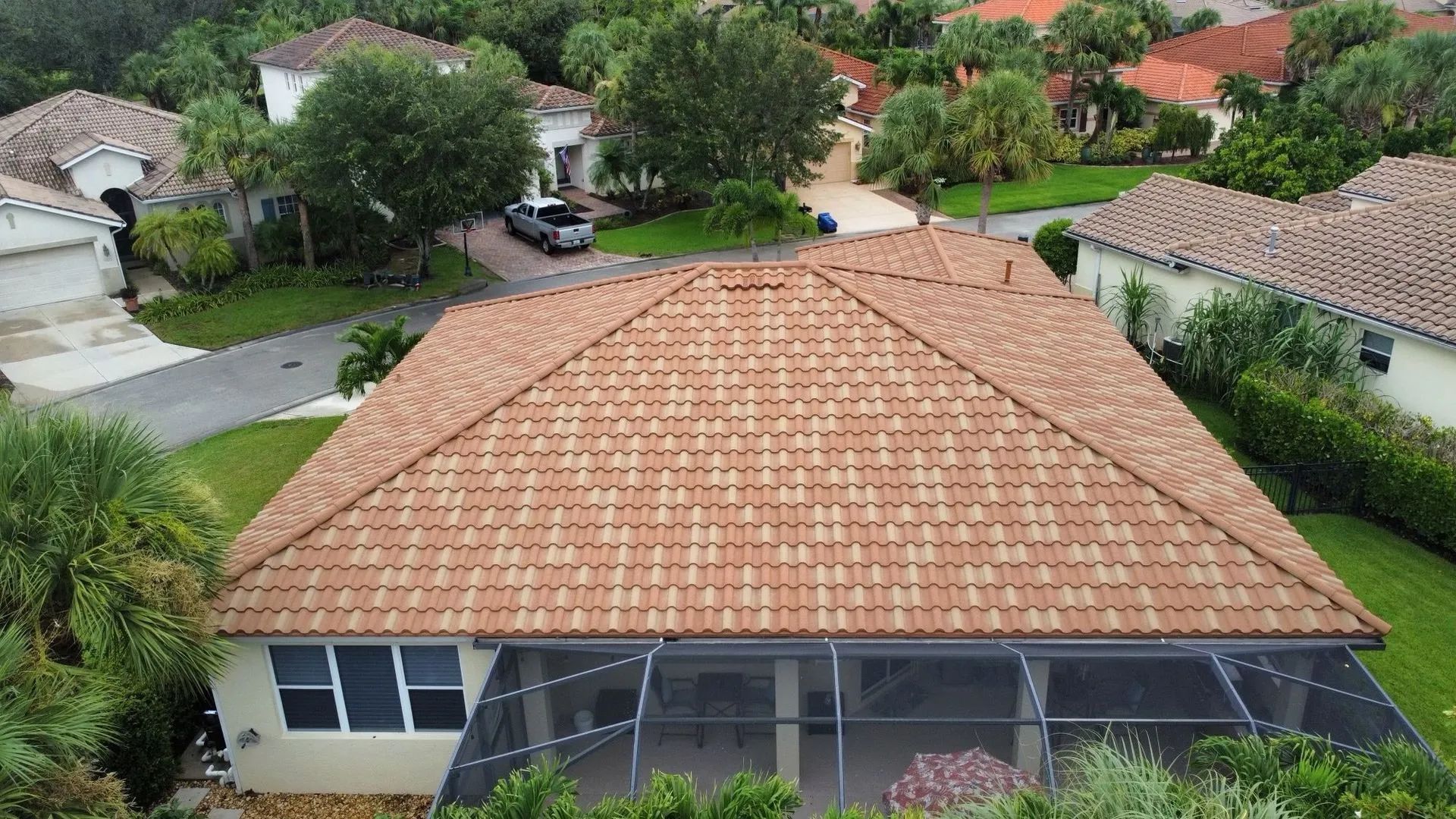 An aerial view of a tan tile roof on a suburban home, featuring a screened-in back patio and surrounding landscaped yards.