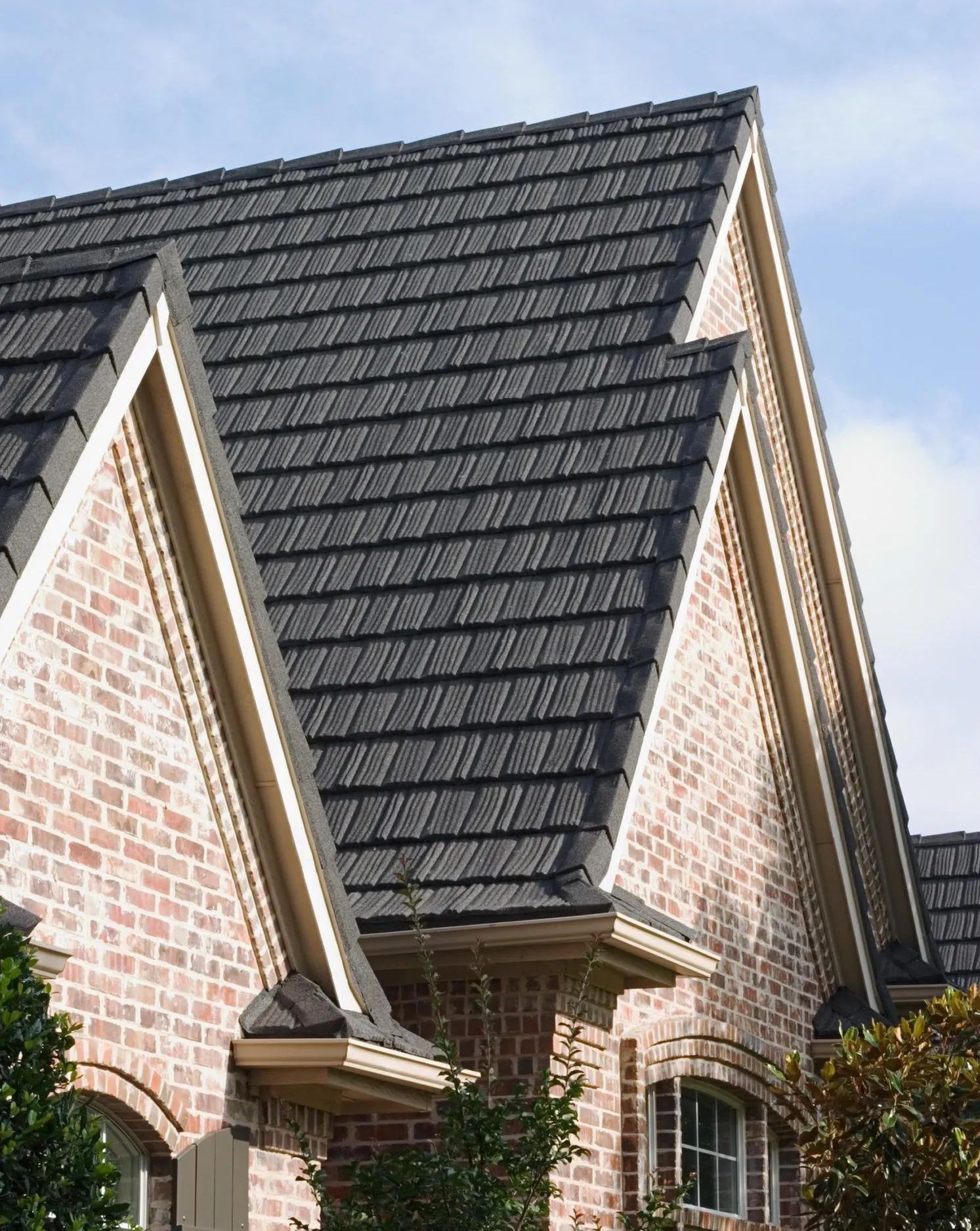 The peaked, grey-tiled roof and red brick facade of a house against a blue sky.