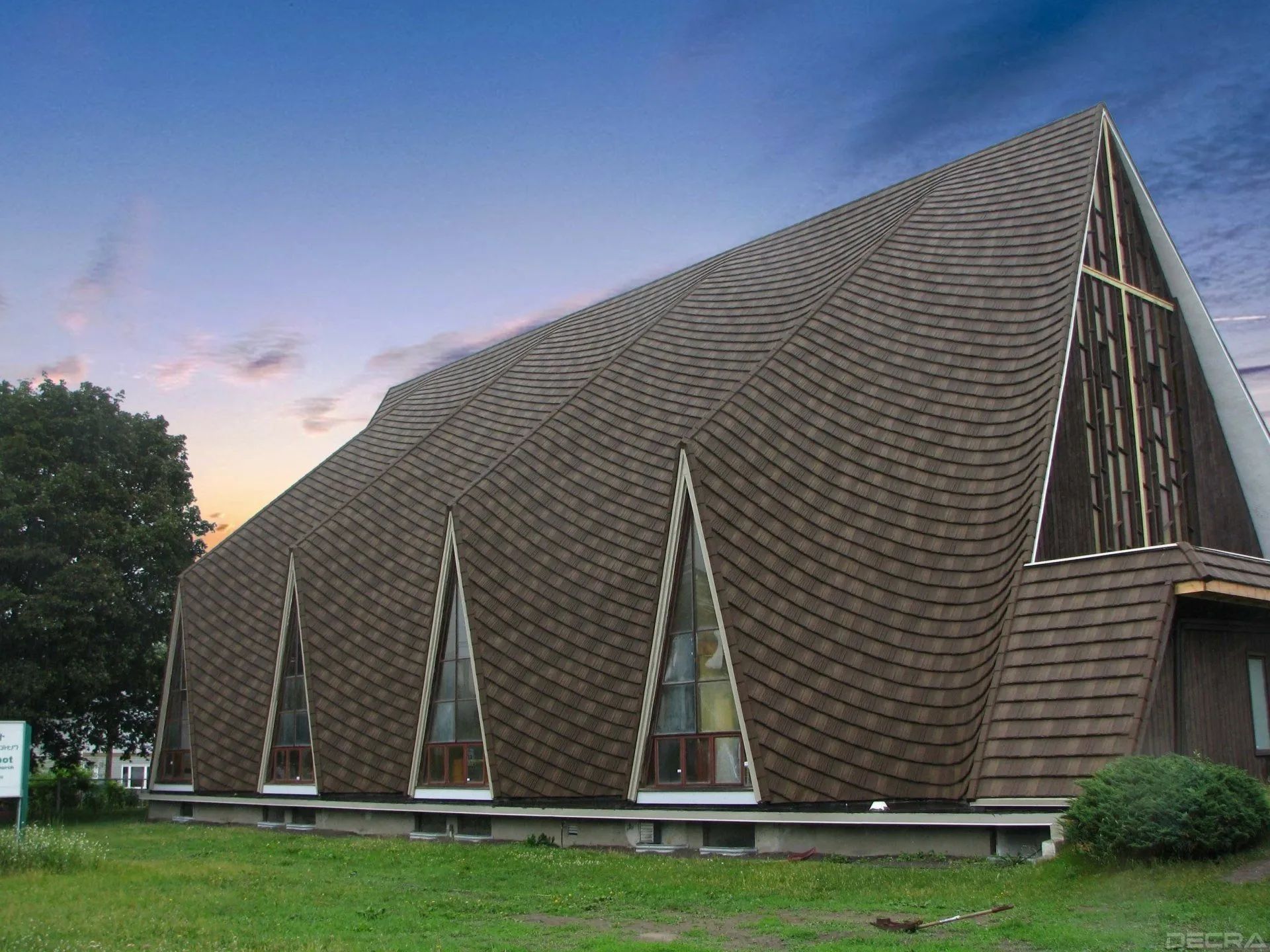 A-frame church building with brown shingles and triangular windows against a sunset sky.