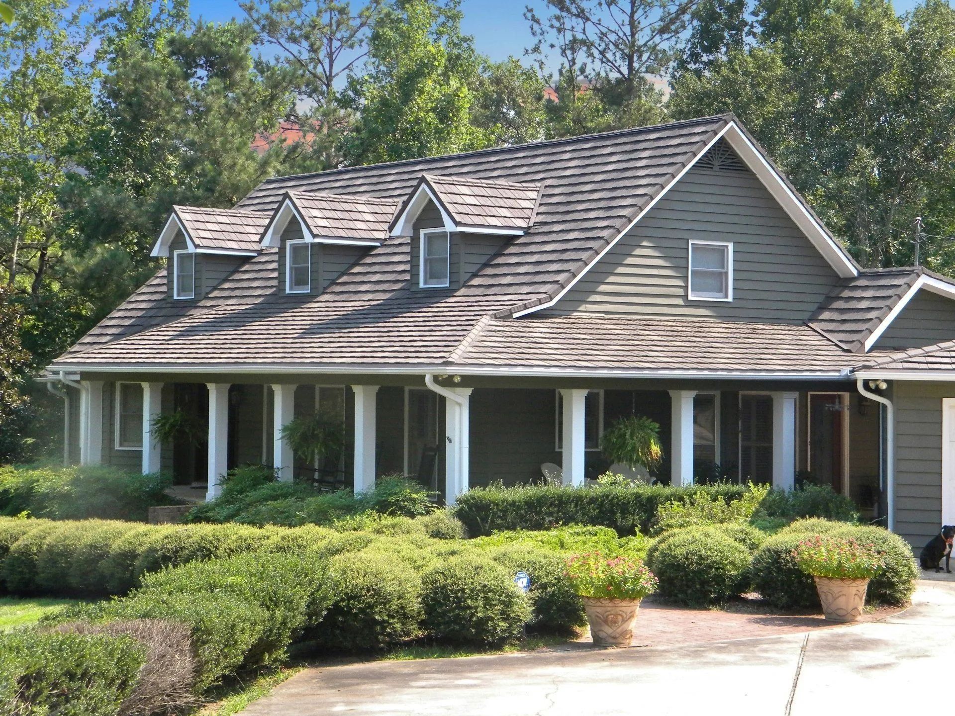 A green house with a dark roof and a pillared porch, surrounded by neatly manicured shrubs and trees.