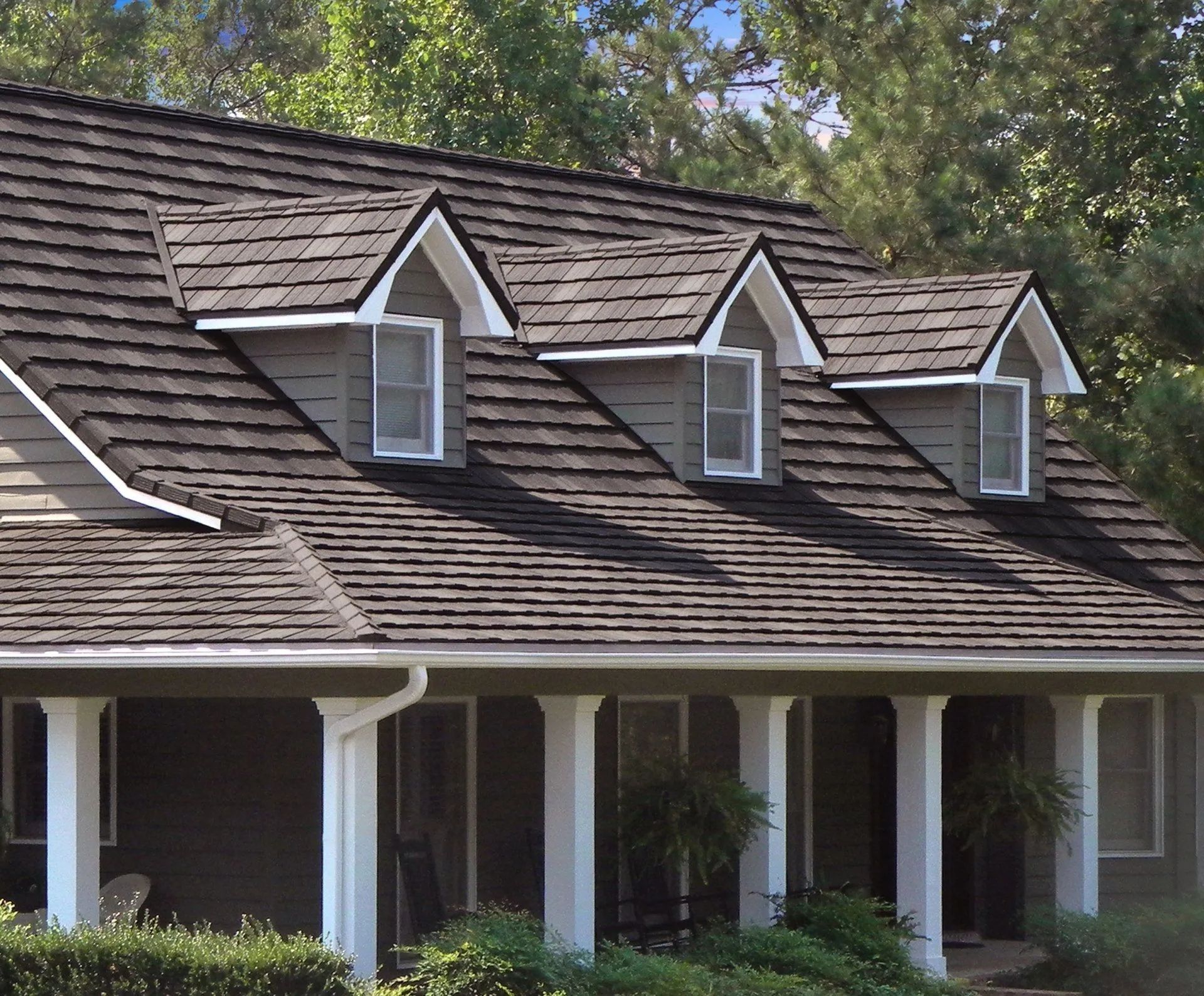 A house exterior featuring a dark brown shingled roof with three gabled dormers above a columned porch.
