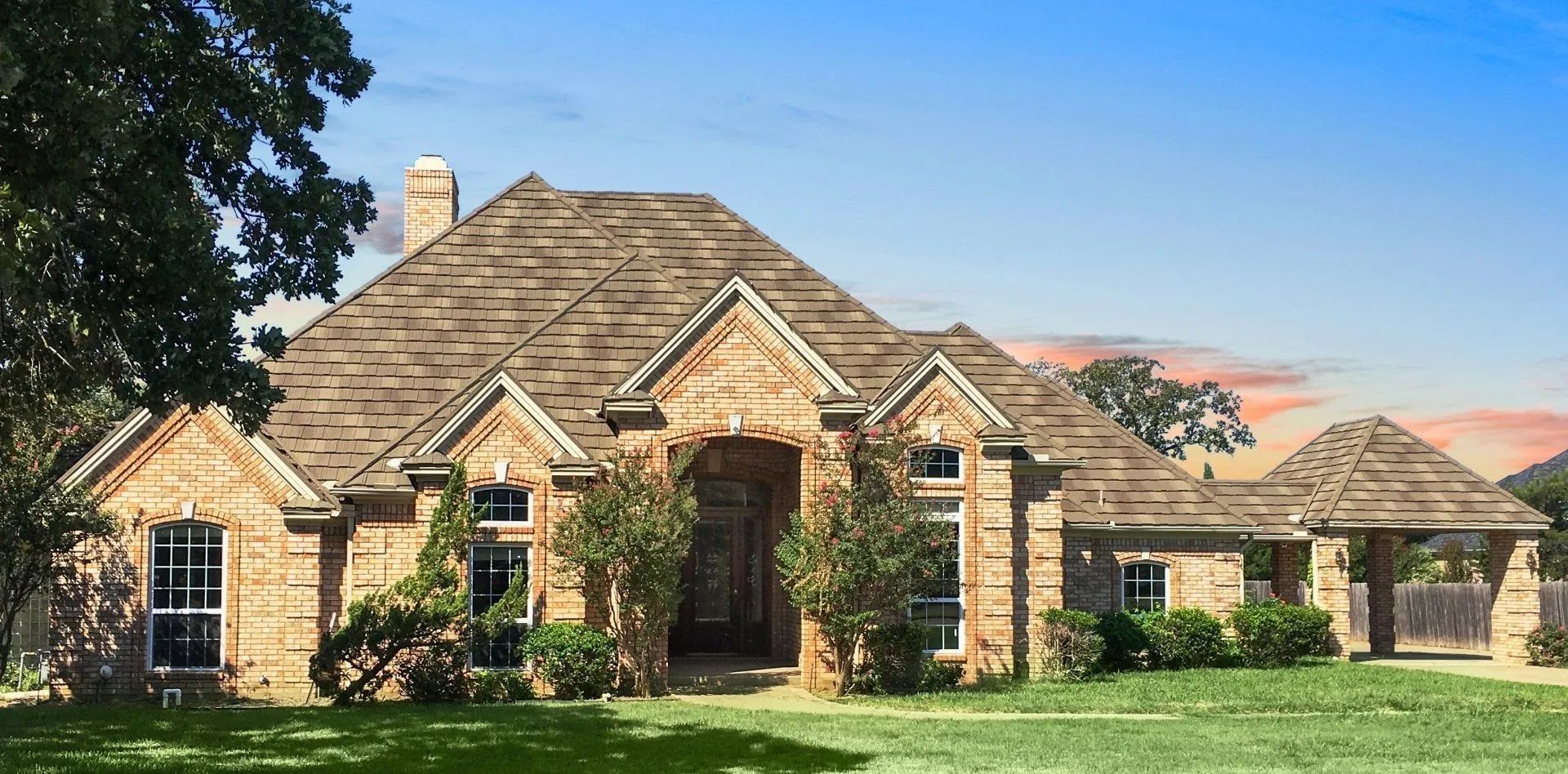 A single-story tan brick house with a complex roofline, gabled windows, and an attached porte-cochere on a grassy lawn.