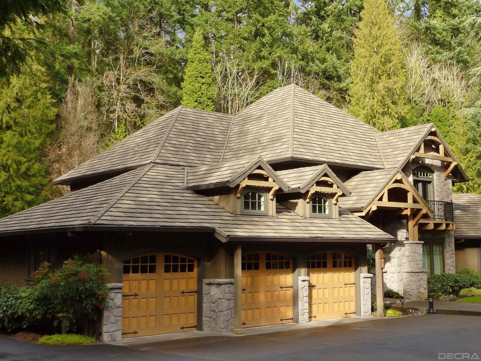A multi-car garage with arched wooden doors, stone pillars, and decorative timber framing, nestled in a wooded setting.