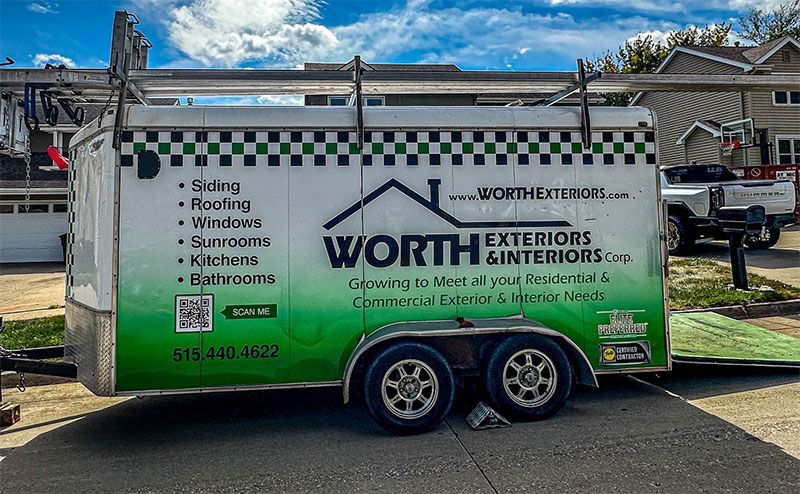A white utility trailer parked on a residential street, branded with green logos for Worth Exteriors & Interiors.