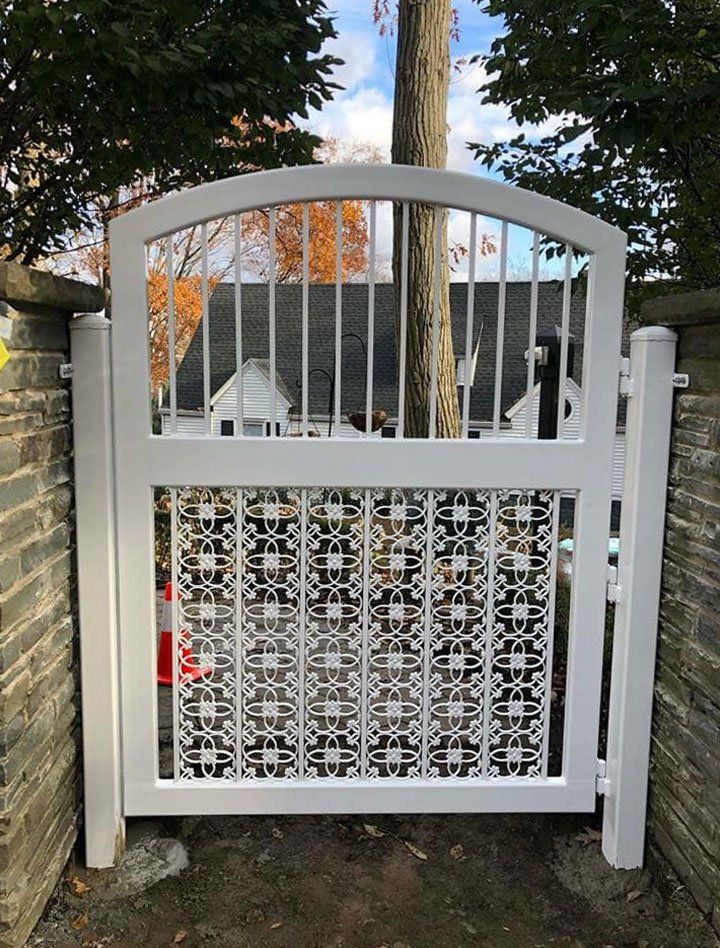 A white gate with a pattern on it is next to a brick wall