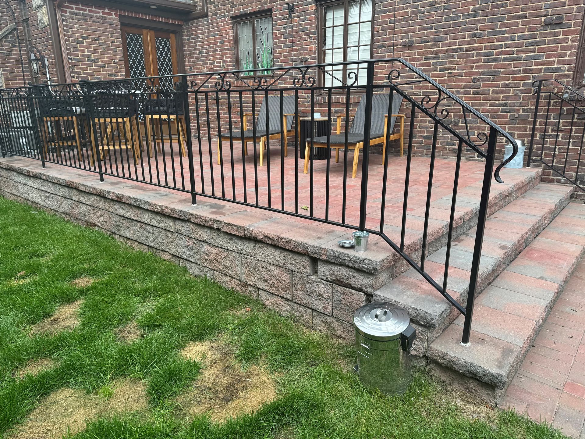 A patio with a wrought iron railing and stairs in front of a brick building.