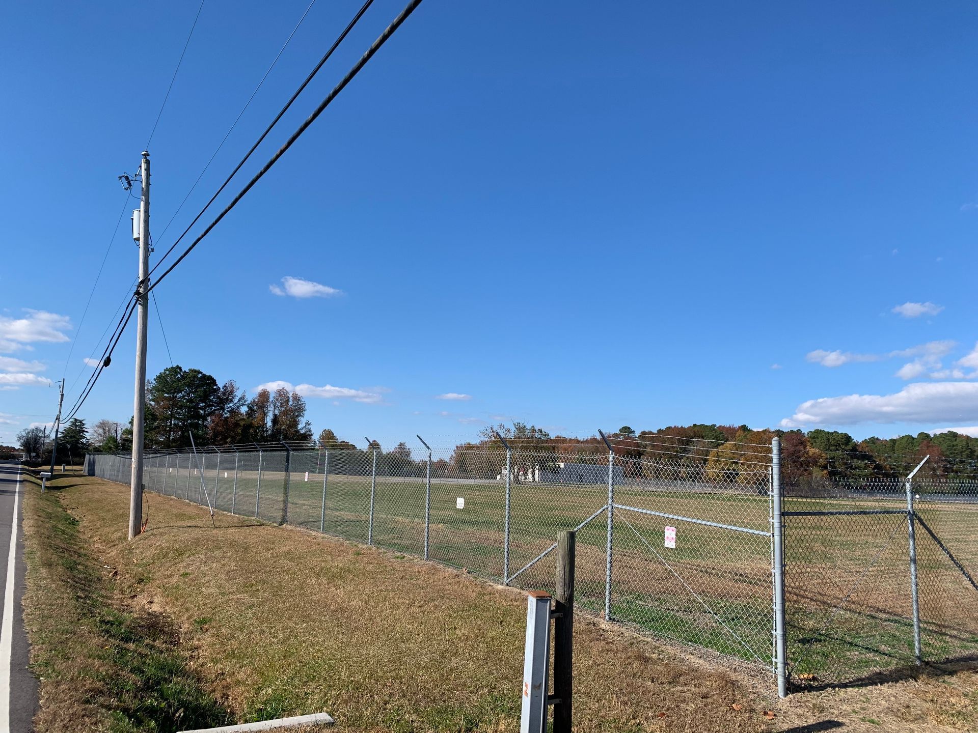 A chain link fence surrounds a field on a sunny day.