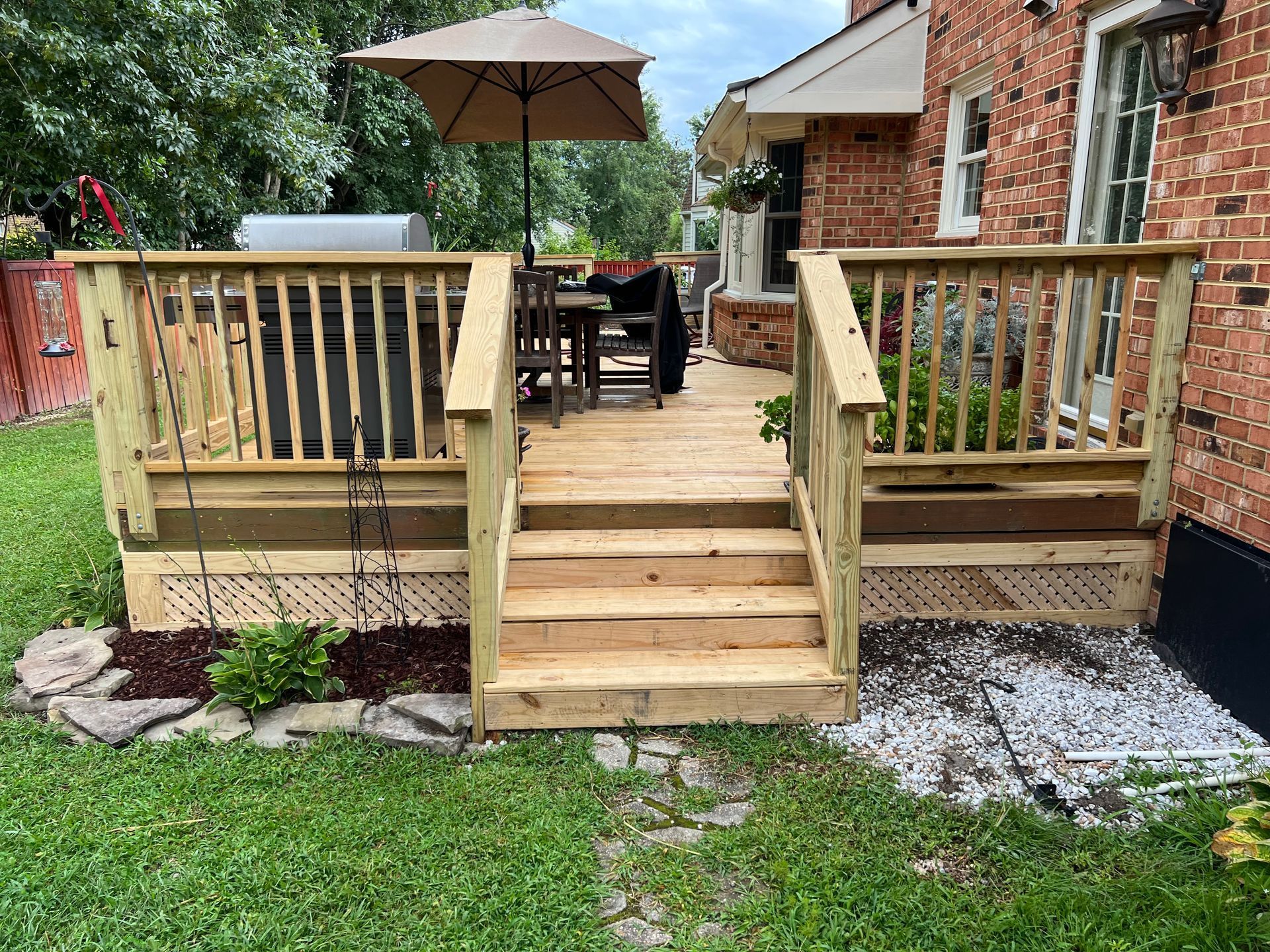 A wooden deck with stairs and an umbrella in front of a brick house.