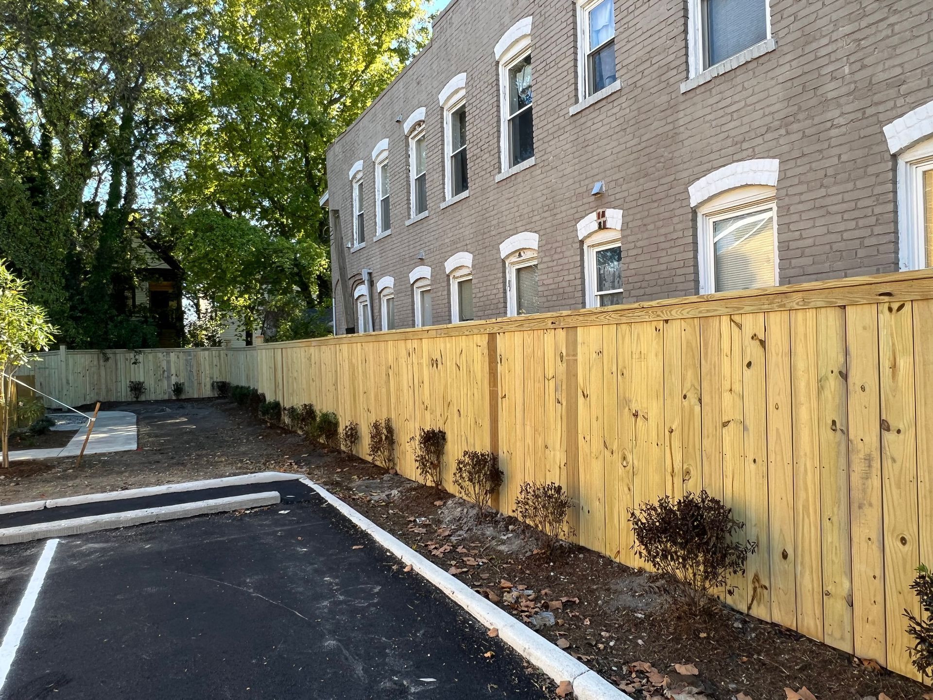 A wooden fence surrounds a parking lot in front of a brick building.