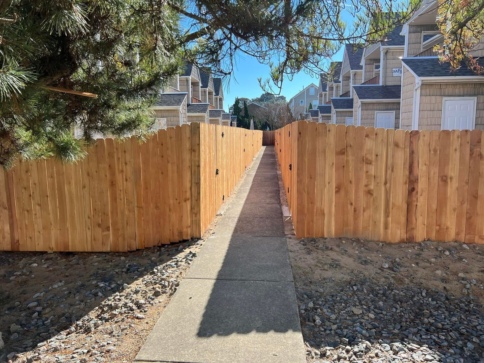 A wooden fence along a sidewalk leading to a row of houses.