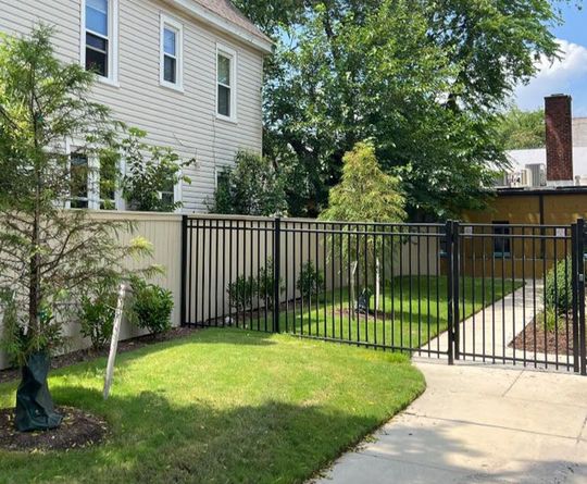 A black fence surrounds a lush green yard in front of a house.