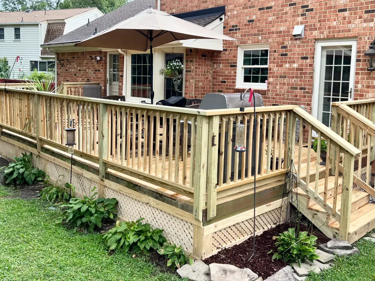 A wooden deck with stairs and umbrellas in front of a brick house.